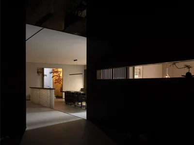 深色調餐廳帶黑色門道，餐桌周圍環繞座椅，以及附水槽與冰箱的廚房區域