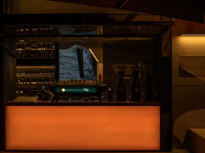 A casual dining environment with an orange bar counter, cups, and a TV mounted above, in a restaurant or cafe setting