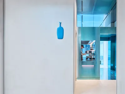 A modern restaurant interior with a counter, glass, and wood, featuring a man standing in front of the counter with two bottles on display