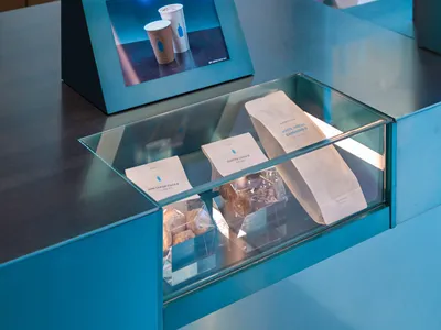 咖啡店櫃檯上擺放杯子、咖啡豆，並有電視螢幕顯示產品資訊