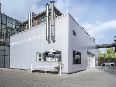 工業建築外觀白色立面，一樓設有現代咖啡廳與餐廳，側邊有管線延伸