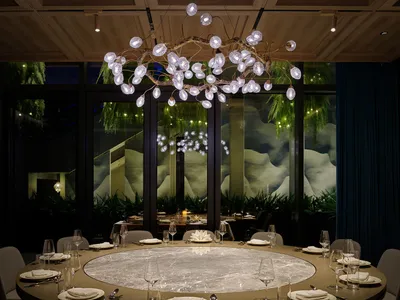 A sophisticated dining space with a large glass table surrounded by chairs, wine glasses, and cups, set in a well-lit room