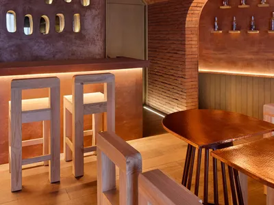 A modern restaurant interior with a brick wall, wooden tables, and a warm ambiance, featuring three chairs and rustic walls