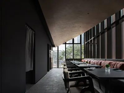 A modern restaurant interior with a large dining table surrounded by chairs, featuring a combination of black and white elements and dim lighting