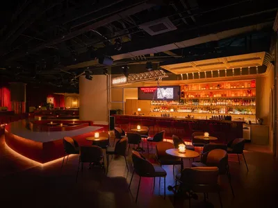 Modern bar and restaurant interior with red walls and flooring, featuring chairs, dining tables, and a large TV screen