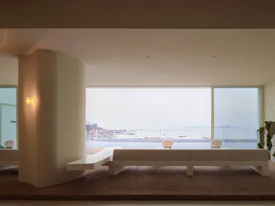 Open living space with large windows offering an ocean view, featuring a bench and two chairs for comfortable seating