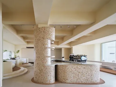 A restaurant interior with a large stone column featuring a unique brick pattern, surrounded by dining tables and chairs, and potted plants, in a well-lit and inviting atmosphere