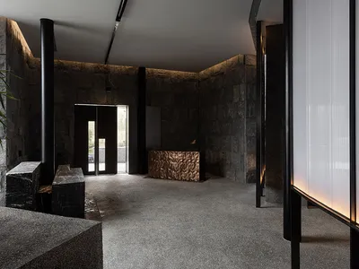 Well-designed hotel lobby with a stone wall, black doorway, and natural light from a circular ceiling window, featuring a bench and potted plants