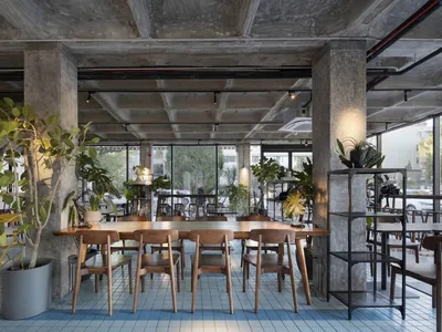 現代餐廳內部，大型木質餐桌環繞金屬椅，搭配盆栽與花瓶，自然光線灑落