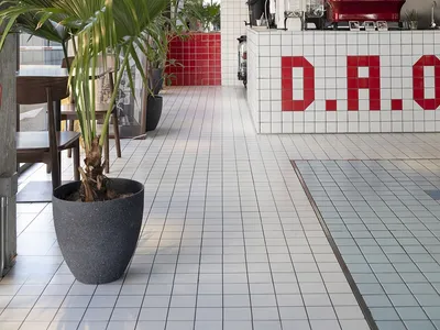 A modern restaurant interior with a counter featuring a coffee machine and sink, surrounded by potted plants and a chair, with a clean and organized atmosphere