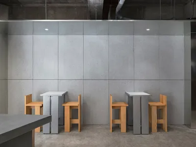 Empty restaurant with two grey tables and wooden chairs in a modern space with concrete walls and a calm atmosphere