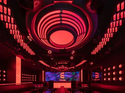A modern restaurant with a circular dining table surrounded by chairs, red lights on the walls, and smaller tables scattered throughout