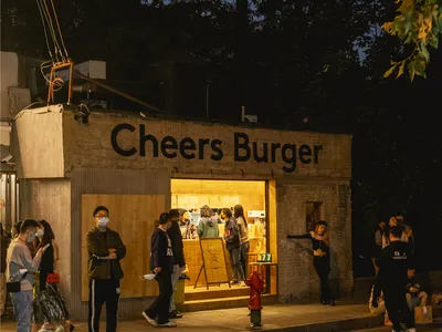 A casual restaurant exterior with a brick wall, people waiting outside the entrance, and a welcoming atmosphere