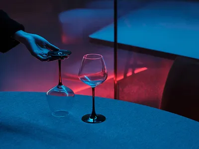 A contemporary dining space with a clear glass table, minimalist decorations, and a unique touch of a remote control in a wine glass