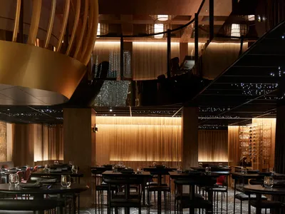 Dimly lit modern restaurant interior with multiple tables and chairs, wine glasses, and a sophisticated atmosphere