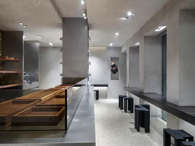 Modern restaurant interior with a large counter, gray and brown tones, stools, and decorative items, highlighted by lighting
