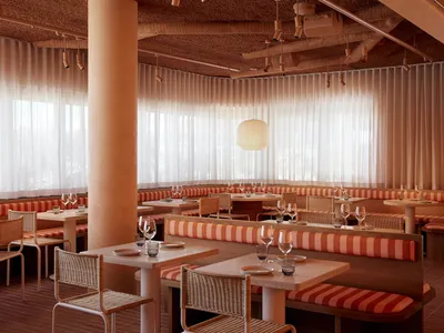 A casual restaurant interior with multiple dining tables and chairs, wooden furniture, and wine glasses on the tables