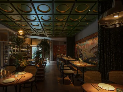 Warm and inviting dining space with multiple tables, chairs, potted plants, and a green and gold color scheme