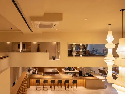溫暖舒適的餐廳內部，木質地板、米色牆面，吧台區設有高腳椅，周圍環繞用餐桌椅