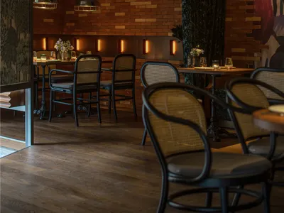 Modern restaurant interior with wooden floor, brick walls, potted plants, and comfortable seating for guests