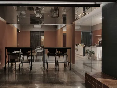 A modern restaurant dining area with three tables and chairs, warm brown and black tones, and well-lit space with natural or artificial light