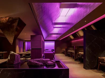 A cozy restaurant dining area with purple walls, ceiling lights, and tables and chairs, creating a warm and inviting atmosphere