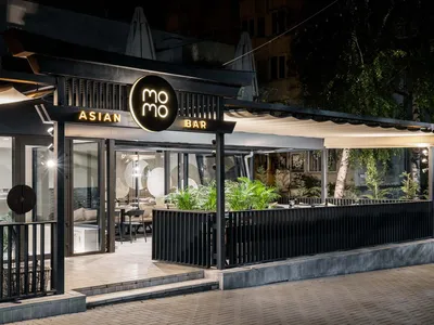 A modern Asian restaurant with a black and white design, featuring tables, chairs, and potted plants, creating an inviting and comfortable atmosphere