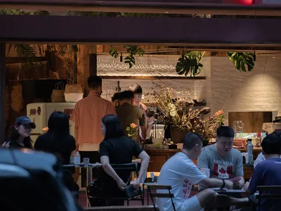 A casual dining space with various chairs and tables, surrounded by potted plants and a relaxed atmosphere
