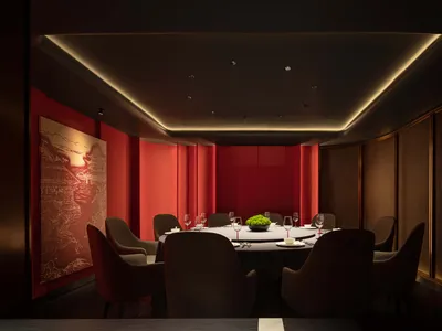 A luxurious dining area with a round table, wine glasses, plates, and cutlery, surrounded by multiple chairs in a warm and cozy red-themed space