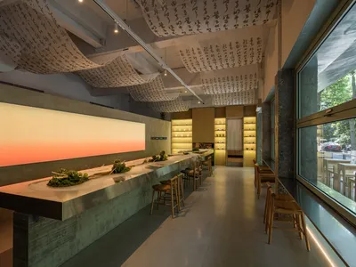 A modern Asian restaurant with a long wooden bar, oriental decorations, and multiple bowls on the counter
