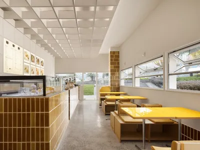 擁有黃色桌椅、白牆壁與金屬吊頂的現代餐廳，自然光線充足，氛圍溫馨誘人