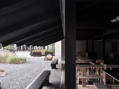 A modern restaurant interior with wooden tables and benches, a black roof, and multiple chairs, creating a warm and inviting atmosphere