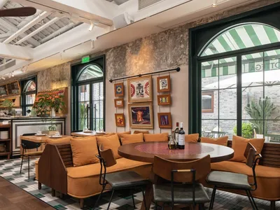 Cozy restaurant dining area with multiple couches and chairs around a large round table, wine bottles on the table, and a warm atmosphere