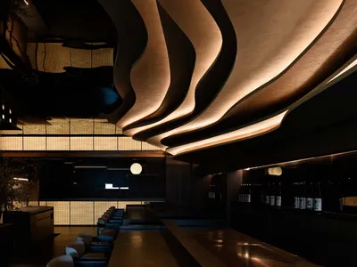 Modern restaurant interior with a bar area and dining space featuring chairs, tables, and bottles, designed to create a comfortable atmosphere for patrons