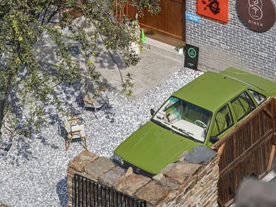 A brick restaurant with a red sign and a green car parked outside, set against a natural background
