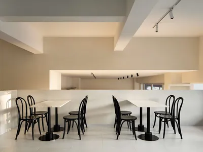 A modern restaurant interior with white walls, several dining tables, and black chairs, creating a bright and airy atmosphere