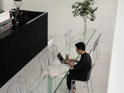 Casual dining space with a glass table, chairs, and people using a laptop and sitting nearby