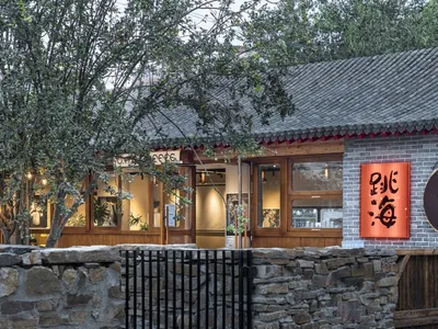A well-lit Asian restaurant with a stone exterior, red roof, large window, and potted plants inside