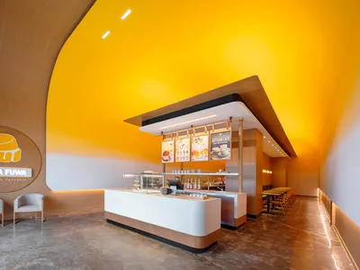 A modern Japanese restaurant interior with a yellow theme, featuring a counter with a cash register and displayed food items, surrounded by cups and a bowl with a spoon