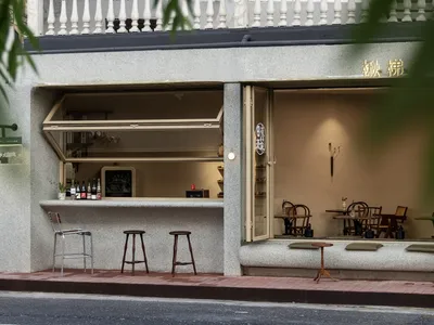 A modern Asian restaurant with a counter and stools, chairs, and potted plants, featuring gray and white tones and warm lighting
