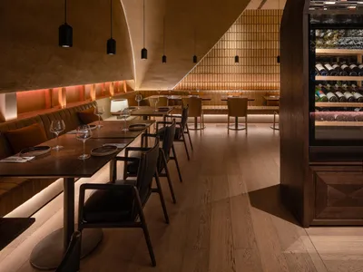 Cozy restaurant interior with tables, chairs, and wine cellar display, creating a sophisticated ambiance