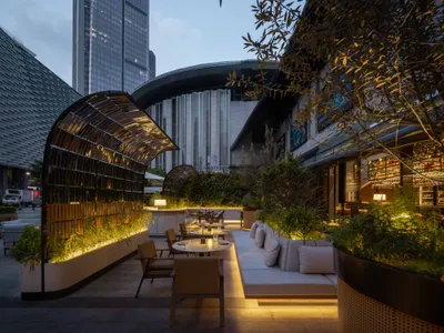 A modern restaurant patio at night with a glass structure, comfortable seating, and a cozy ambiance