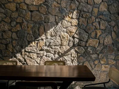 A warm and inviting dining area with a wooden table and chairs, surrounded by a stone wall and natural light