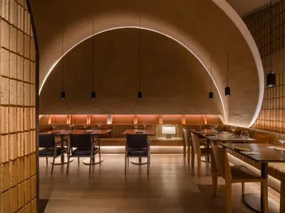 A warm and inviting dining area with a curved ceiling, multiple tables, and chairs, featuring wood and glass elements