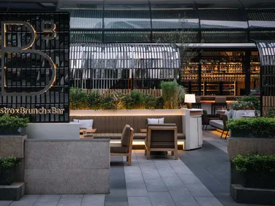 A modern restaurant with a bar area, chairs, and dining tables, surrounded by potted plants, creating a comfortable atmosphere for patrons