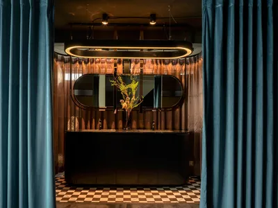 Sophisticated hotel lobby bar with a large mirror, potted plants, and decorative vases, set against a backdrop of black accents and inviting atmosphere