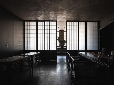 A dimly lit, modern restaurant with a black and white theme, featuring a large dining table and chairs, creating a cozy atmosphere