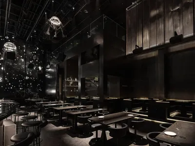 深色調親密的音樂餐廳內部，設有多張餐桌、椅子與酒杯，營造溫馨氛圍