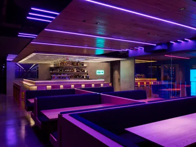A modern restaurant bar area with purple accents, multiple tables, and comfortable seating options