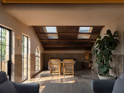 A warm and inviting living area with a dining table under a skylight, surrounded by chairs and a potted plant, with natural light filling the space